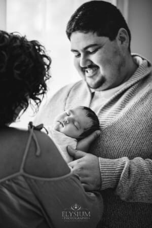 A father smiles down at the sleeping newborn baby as she lays comfortably in his arms