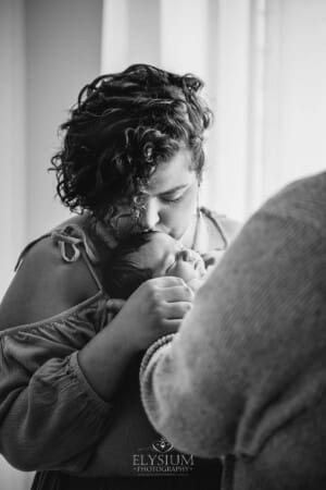 A mother kisses her newborn baby on the head as she lays sleeping in her arms