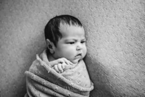 An awake newborn baby laying on a textured blanket, black and white image