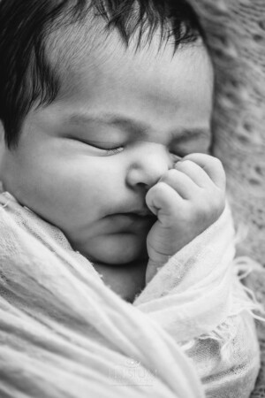 A newborn baby sleeps wrapped in a white blanket with her hand on her cheek