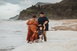 A family stand on a beach kicking waves and laughing