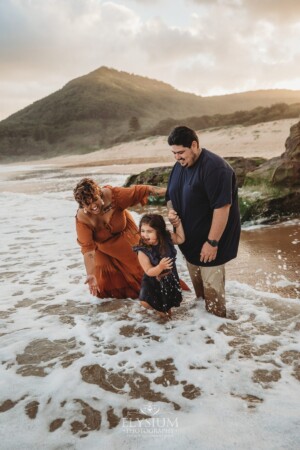 A family stand on a beach as a wave washes up at sunset and they splash eachother