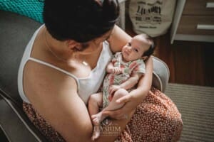 A mother sits in an armchair and cuddles her newborn baby girl in her arms