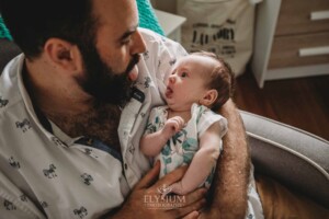 A father cuddles his newborn baby boy as they both poke out their tongues