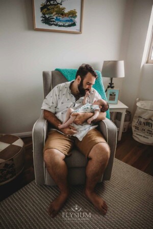A father sits in a rocking chair holding his newborn baby
