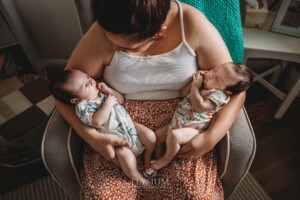 A mother sits in a chair holding her newborn twins in her arms