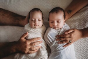 Parents hold their newborn twins between them as they lay on a patterned white blanket