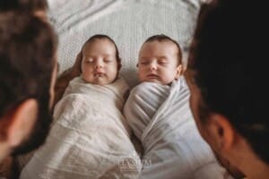 Parents hold their newborn twins between them as they lay on a patterned white blanket