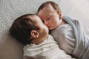 Newborn twins lay wrapped with their little noses pressed together