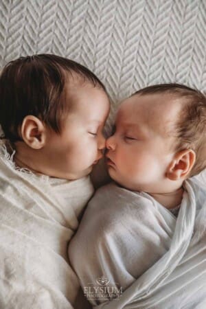 Newborn twins lay wrapped in white with their little noses pressed together