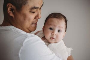 A baby boy wrapped in a white blanket is held lovingly by his father