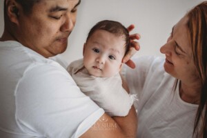 A newborn baby is held by his parents as they stroke his little head