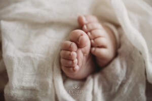 Tiny newborn baby feet poke out the end of a white wrap