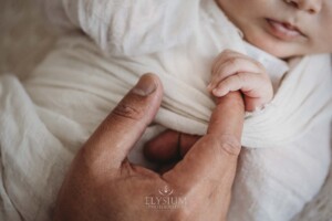 A tiny newborn baby's hand holds his fathers finger
