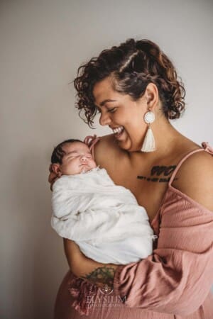 A mother smiles at the sleeping newborn baby in her arms