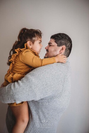A kid cuddles her daddy as he holds her in his arms and they both smile