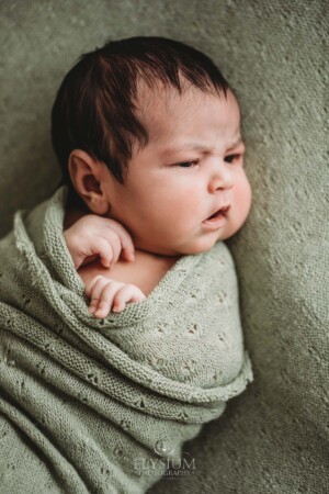 A newborn lays awake on a green textured blanket and matching wrap