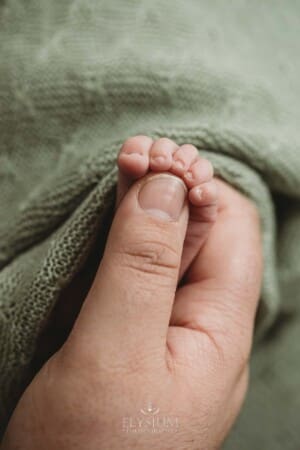 A dad presses his thumb against his newborn baby's tiny foot to show the scale of his little child