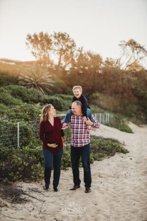 A pregnant woman walks along a beach with her family at sunset