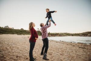 A little boy is tossed in the air by his dad as his pregnant mum watches on