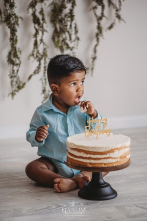 A baby boy puts a piece of cake into his mouth during his cake smash session