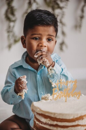 A baby smashes cake into his mouth sitting in a bright studio
