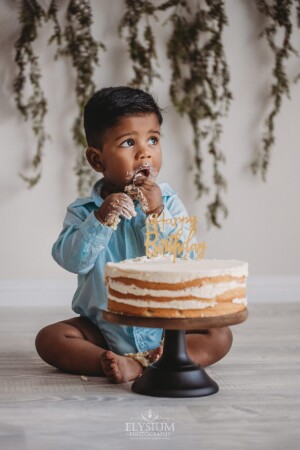A baby boy sits in a studio with his birthday cake as he makes a mess