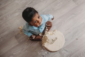 A baby boy sits on a studio floor covered in cake as he smashes it with his hands