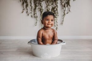 A baby boy sitting in a studio tub getting clean after his cake smash session