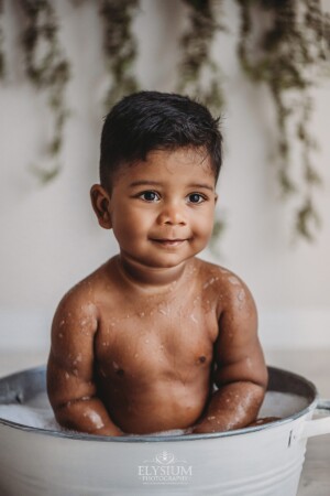 A smiling baby boy sitting in a tub filled with bubbles