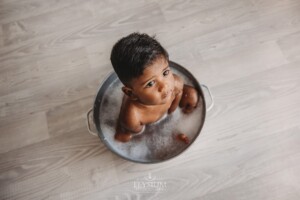 A baby boy sits in a white vintage tub filled with bubbles