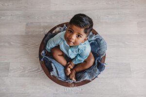 A baby boy sitting in a wooden bowl prop with a blue outfit