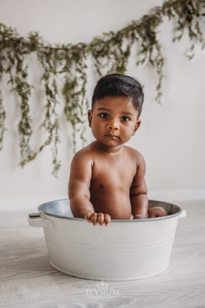 A baby sits in a white bathtub to clean off his cake smash mess