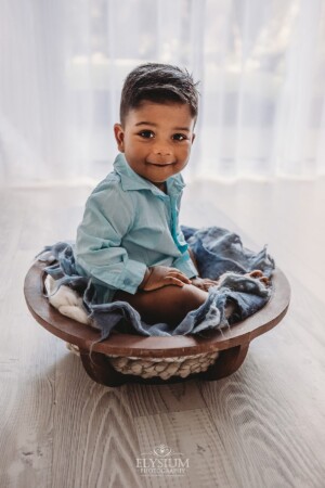 A baby boy sits in a studio prop with a bright window behind him