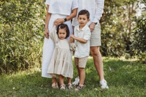 Kids stand between their parents and hold their hands in a green field