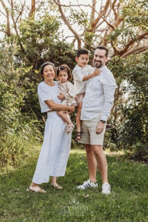 Parents hold their small children as they stand in a tree lined green field