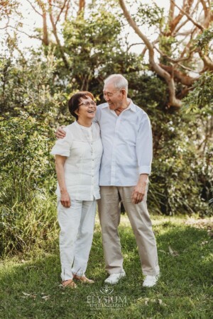 An elderly couple stand in a bushy park and giggle at each other