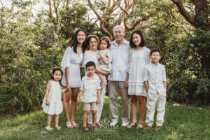 An elderly couple stand in a grassy park surrounded by their grandchildren at sunset