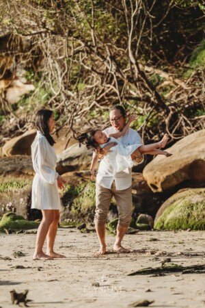 A couple stand on a sandy beach and play with their little girl