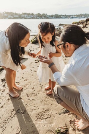 Parents show their little girl a sea shell as they stand on a beach at sunset