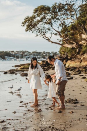 A family walk their little girl along the shoreline at sunset