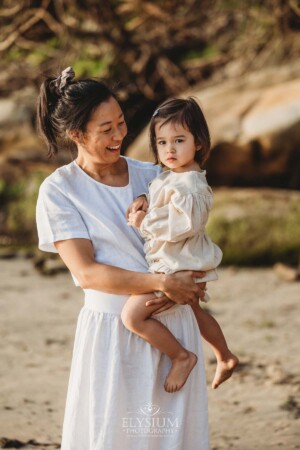 A mother cuddles her baby girl as they stand on a beach at sunset