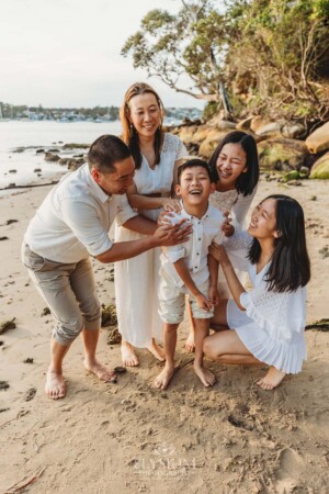 A family stand cuddled together laughing on a beach at sunset