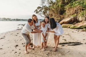 A family stand cuddled together laughing on a beach at sunset