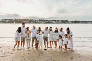 A family stand on the sand at a beach with the sun setting behind them