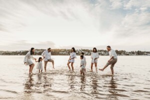 A large family group kick water at each other on a beach at sunset