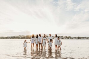 A large family stand together in shallow water as the sun sets behind them