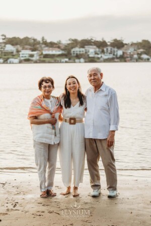 Parents stand with their adult daughter on the shoreline at sunset