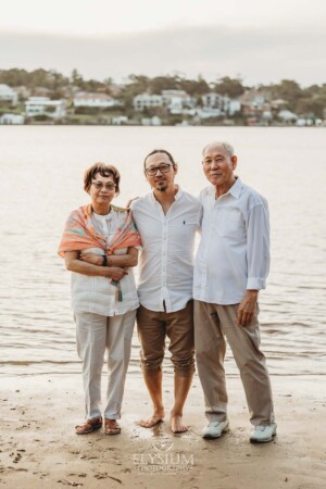 Parents stand with their adult son on the shoreline at sunset