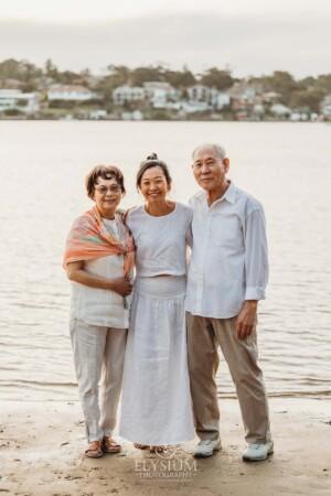 Parents stand with their adult daughter on the shoreline at sunset